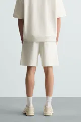 Bermuda de algodón color beige claro, corte relajado (relaxed fit), con cintura elástica ajustable mediante cordón y bolsillos laterales y trasero de plastrón.