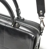 Cartera estilo baúl de cuero negro con doble asa de mano, correa ajustable y extraíble, y placa metálica con logo en el frente.