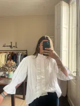 Camisa marrón de cuello alto con volados, mangas abullonadas y puños elásticos fruncidos. Cuenta con una tira de volados en la parte frontal.