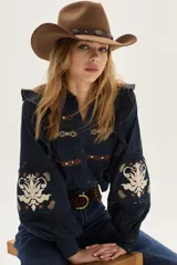 Blusa azul marino de algodón con volados en los hombros, mangas largas abullonadas y detalles de bordados florales y geométricos en el pecho y las mangas.