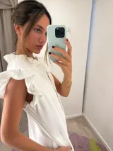 Vestido midi de color blanco con escote en V, cierre frontal abotonado y mangas cortas con volados. Presenta un diseño fluido con falda evasé y detalle de volado en el ruedo.