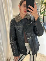 Campera tipo gamulán de cuero genuino color negro, con interior y cuello de piel sintética en tono grisáceo. Presenta cierre frontal, costuras visibles y diseño estructurado.