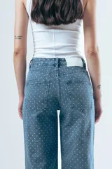 Pantalón de jean corte wide leg, color beige con estampado de rayas verticales finas. Presenta tiro alto, cierre frontal con botón y bolsillos laterales.