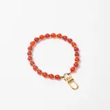 Colgante para cartera compuesto por cuentas esféricas de color rojo intercaladas con pequeñas arandelas doradas, finalizado con un mosquetón metálico dorado.