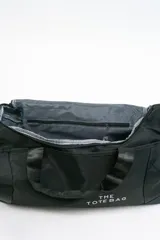 Bolso de viaje gris con doble asa corta y cierre superior. Estampado frontal con la frase "The Tote Bag" en letras blancas.