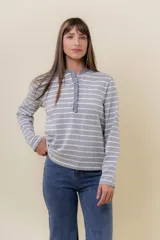 Remera de manga larga con diseño a rayas horizontales en gris y blanco. Presenta un cuello redondo con detalle de volado a lo largo de la cartera frontal con botones.