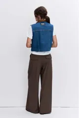 Chaleco de denim azul con cuello camisero en contraste color marrón, cierre frontal con botones metálicos y bolsillos superiores con solapa.