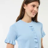 Camiseta de punto celeste con cuello redondo, mangas cortas y cierre frontal de botones, adornada con volantes en la botonadura, los puños y el dobladillo.