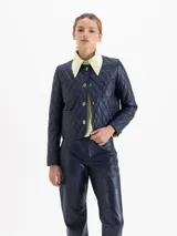 Chaqueta de cuero vacuno azul marino con diseño matelaseado, cuello camisero, cierre frontal con botones metálicos y bolsillos frontales superiores e inferiores.