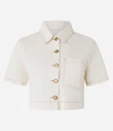 Camisa cropped de sarga color crudo, con cuello clásico, cierre frontal con botones dorados, manga corta, bolsillo de parche en el pecho y costuras a contraste. Confeccionada con algodón certificado.