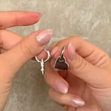 Par de caravanas tipo argolla con dije colgante en forma de corazón, con borde lateral decorado con pequeñas piedras brillantes.