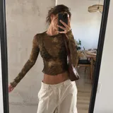 Top de microtul verde con estampado abstracto, manga larga y cuello redondo. Presenta terminaciones con dobladillo ondulado en el cuello, los puños y el ruedo.