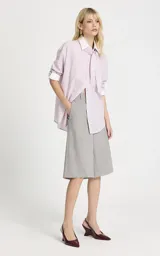 Camisa de algodón con estampado de rayas verticales en tonos rosa y blanco. Presenta cuello clásico, mangas largas con puños anchos en contraste y un detalle de pañuelo integrado en el cuello que simula una corbata. Posee cierre frontal de botones y corte recto.