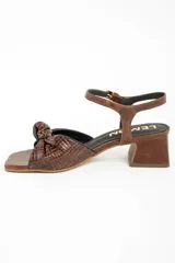 Sandalias de cuero marrón con taco cuadrado medio, tira en el tobillo con hebilla ajustable y diseño trenzado con nudo en la parte delantera.