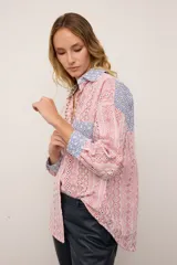 Camisa de corte oversized confeccionada en broderie de algodón con diseño combinado. Presenta un estampado de rayas verticales en tonos rojos y blancos, con detalles en contraste de color azul en el cuello, los puños y el bolsillo frontal. Posee cierre frontal con botones y mangas largas.