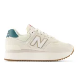 Championes urbanos New Balance modelo 574, color crema con detalles en blanco, verde y marrón, confeccionados en gamuza y malla, con logo "N" característico en los laterales y entresuela alta.