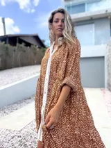 Vestido camisero de corte holgado y diseño escalonado, con estampado de pequeñas manchas blancas sobre fondo terracota. Presenta cuello camisero, cierre frontal con botones y mangas largas con puños.