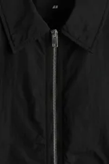 Campera negra de nylon levemente acolchada, con cuello y cierre frontal plateado. Presenta bolsillos insertados al bies y un bolsillo interior con botón a presión. Posee cordón elástico ajustable en el bajo.