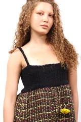 Top de diseño artesanal con cuerpo superior tejido en crochet negro y parte inferior de corte peplum en tejido plano de telar con trama a cuadros en tonos oscuros, rojo y amarillo.