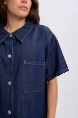 Vestido corto de jean azul oscuro, sin mangas, con cierre frontal de botones metálicos y corte ligeramente evasé.