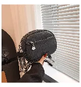 Cartera bandolera color gris claro, de cuero sintético, con correa ancha de tela estampada y cierre superior con cremallera.