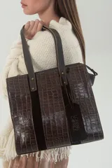Cartera tipo tote de cuero vacuno color chocolate, con textura croco y detalles de descarne agamuzado y cuero graneado en tonos marrones. Tiene doble asa fija, correa larga regulable y desmontable, cierre metálico superior, forro textil con bolsillos internos y herrajes metálicos en níquel envejecido.