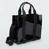 Cartera tipo shopper Melissa Dulce, color negro, de material efecto charol. Cuenta con doble asa de mano y correa cruzada regulable de tela con la marca estampada.