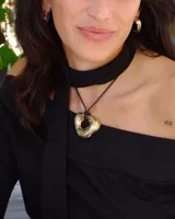 Collar con dije de forma irregular en tonos dorados y plateados, suspendido de un cordón doble de algodón negro.