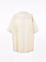 Camisa de manga corta color blanco roto con textura de tejido de lino o similar, corte holgado y cuello camisero.