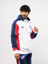 Campera deportiva Umbro del Club Nacional de Football, con cierre frontal, capucha ajustable con cordones y diseño en bloques de color azul, celeste y blanco. Presenta el logo de la marca y el escudo del club bordados en el pecho.