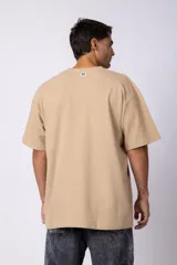 Remera de corte oversized en color marrón, confeccionada en tejido de algodón con textura de micropanal. Presenta cuello redondo con detalle de costura en forma de X y mangas cortas de estilo caído.
