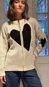 Campera tejida en hilo color crudo con diseño de corazón negro central, cierre frontal completo y detalles bordados en rojo y negro en mangas y cuerpo.