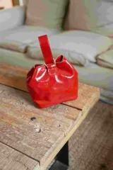 Mini cartera tipo limosnera de cuero charolado en color rojo, con diseño estructurado, cierre superior y asa corta para llevar en la mano o en la muñeca.