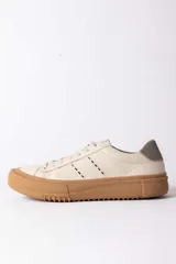 Championes urbanos de cuero en color crema con suela de goma gruesa en tono caramelo. Presentan detalles de costuras decorativas en el lateral y un refuerzo en el talón en color gris.