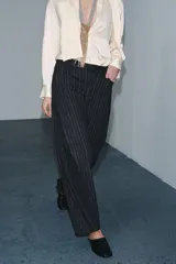 Pantalón de tiro medio con diseño balloon, confeccionado en tejido con patrón de rayas verticales. Presenta cintura con trabillas, cierre frontal con cremallera y botón, y cinco bolsillos.