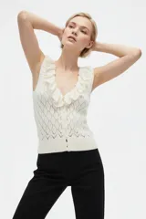 Top de punto color blanco natural, sin mangas, con escote en V pronunciado decorado con volados fruncidos. Presenta cierre frontal con pequeños botones y diseño texturizado en rombos.