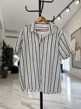 Camisa de manga corta de corte oversize en color blanco con rayas verticales negras, cuello camisero y cierre frontal con botones.