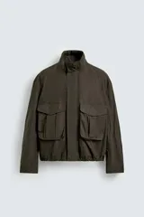 Cazadora de corte cropped confeccionada en algodón con acabado encerado. Presenta cuello subido, cierre frontal con cremallera oculta por solapa con botones a presión, bolsillos de plastrón con solapa en el delantero y bajo ajustable con elástico interior.
