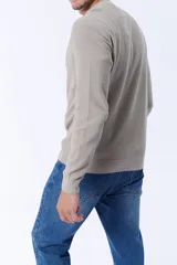 Buzo de punto en color taupe, con cuello redondo y textura acanalada. Presenta mangas largas y puños ajustados, ofreciendo un diseño clásico y versátil.