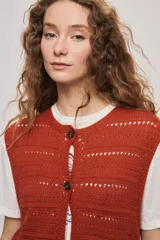 Chaleco de punto color beige, sin mangas, con escote redondo y cierre frontal con botones carey. Presenta diseño calado y silueta amplia.