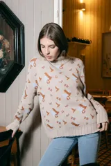 Polera de tejido de punto con cuello alto, diseño holgado y estampado jacquard con motivos geométricos y figuras en tonos beige, naranja y celeste.