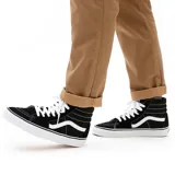 Championes Vans modelo Sk8-Hi de caña alta, color negro con la icónica banda lateral blanca, cordones blancos y suela de goma vulcanizada.