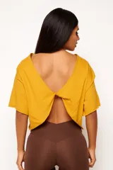 Remera corta de manga corta color celeste, con escote amplio en la espalda que se anuda en la parte inferior, dejando ver un top deportivo amarillo con tiras cruzadas.