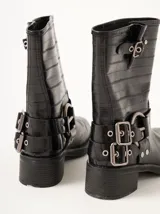 Botas de caña media confeccionadas en cuero texturado color marrón. Presentan un diseño robusto con múltiples hebillas metálicas ajustables, apliques circulares laterales y punta cuadrada. Cuentan con un taco cuadrado de 5 cm de altura.