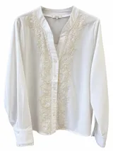 Camisa blanca de manga larga con cuello en V y cierre frontal con botones. Presenta delicados bordados en tonos beige a lo largo de la abertura frontal y el cuello.