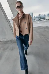 Chaqueta corta de paño en color beige, con cuello subido, manga larga y cierre frontal cruzado con botones oscuros. Presenta bolsillos delanteros de vivo.