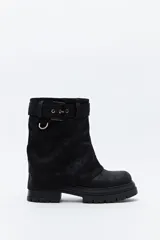 Bota de caña media color negro, con suela robusta dentada y detalle de hebilla ajustable en la parte superior. Presenta una argolla metálica lateral y un diseño de estética urbana con acabado texturizado.