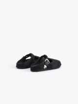 Zueco negro de pelo vacuno, estilo cerrado con abertura en forma de T en el empeine, asegurado con una tira de cuero y hebilla metálica. Incluye un dije metálico con forma de llama en la tira.