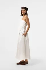 Vestido largo blanco con escote strapless y cuerpo fruncido. Posee falda amplia y fluida con bolsillos.
