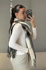 Bufanda rectangular de tejido suave con diseño de cuadros escoceses en tonos mostaza, blanco y gris, terminada con flecos en los extremos.